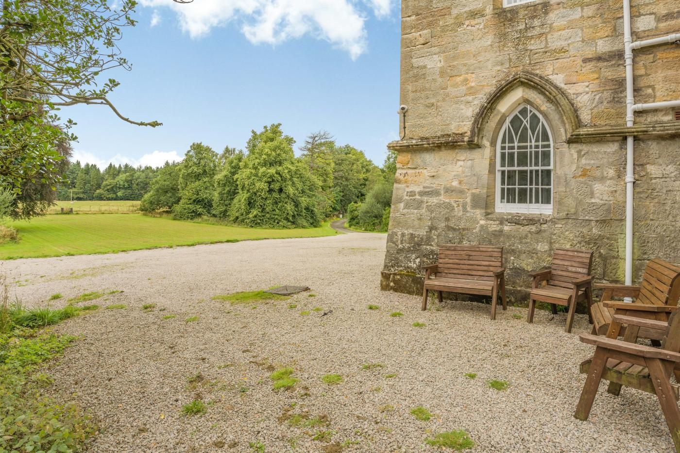 A stone building with a window and a gravel path leading to a seating area with wooden benches.