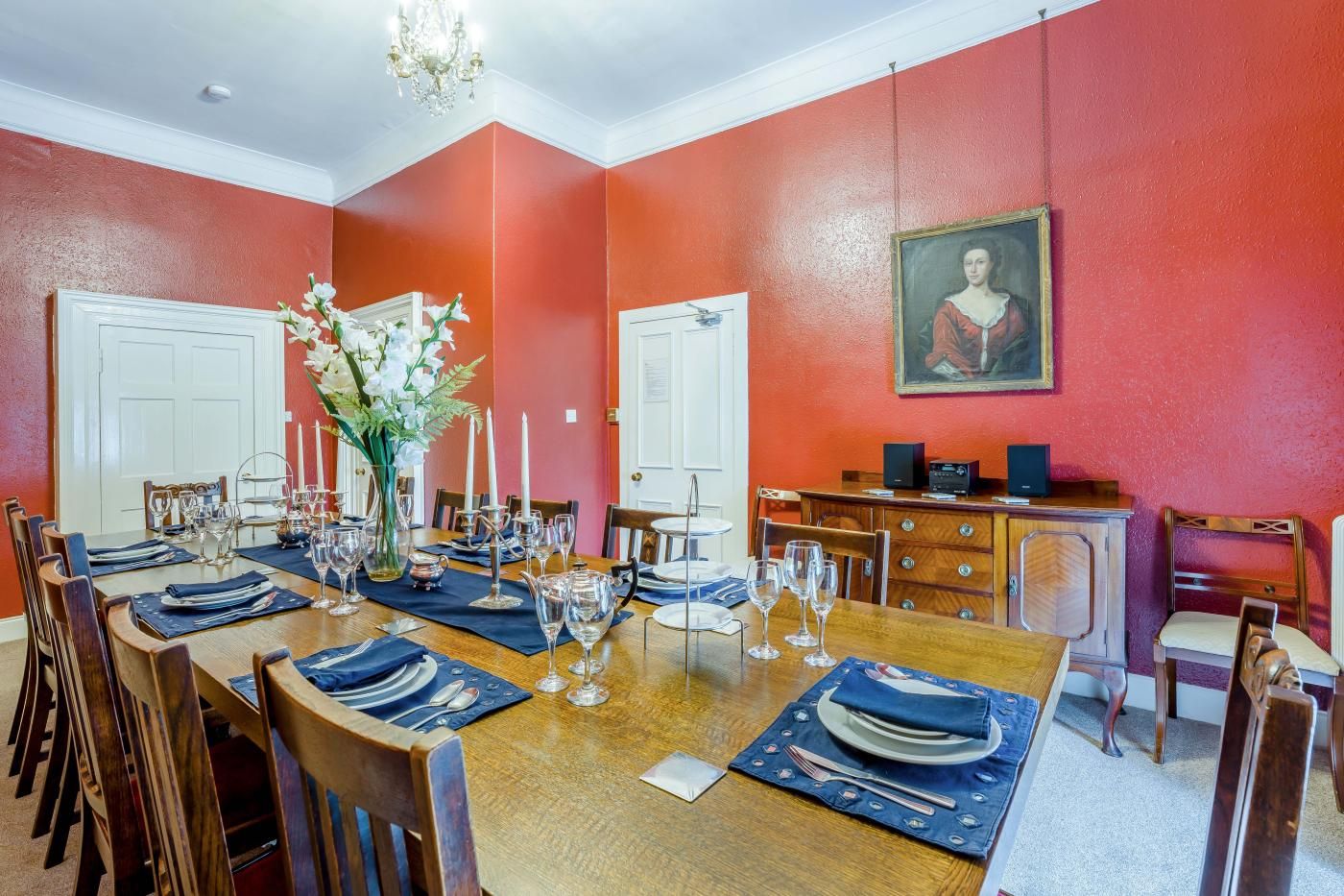 A dining room with a wooden table set for a meal, red walls, and a painting on the wall.