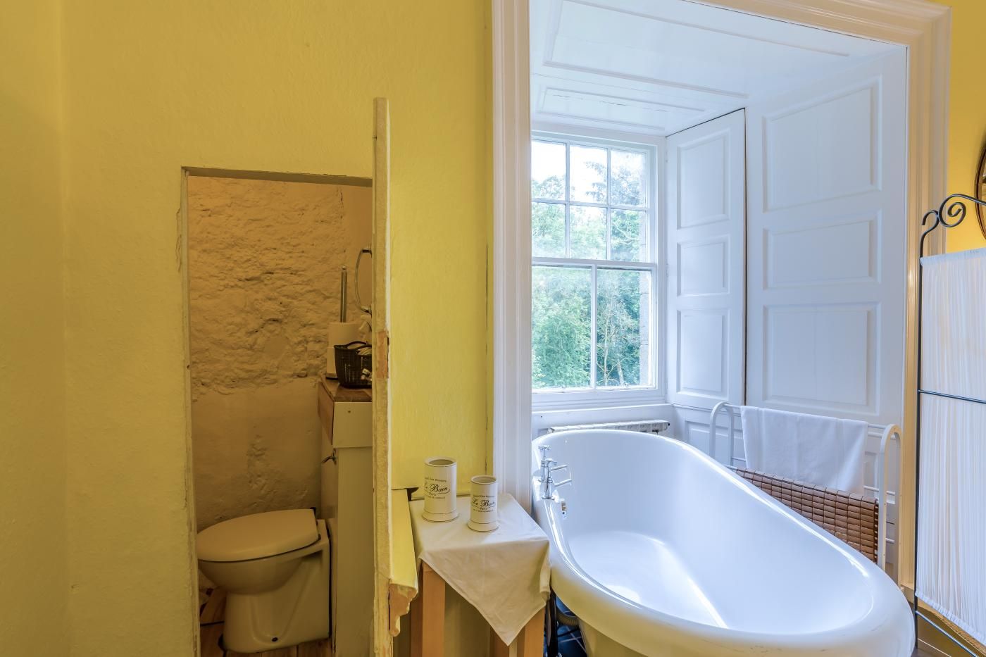 A bathroom with a bathtub, toilet, and a window providing a view of trees.
