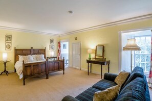 A room with a bed, a sofa, a table with a lamp, and a mirror.