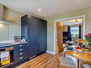 A modern kitchen with dark cabinets, a built-in oven, and a dining area with a wooden table and chairs. - 2 Bed in Richmond (oc-94997) (Kirby Hill)