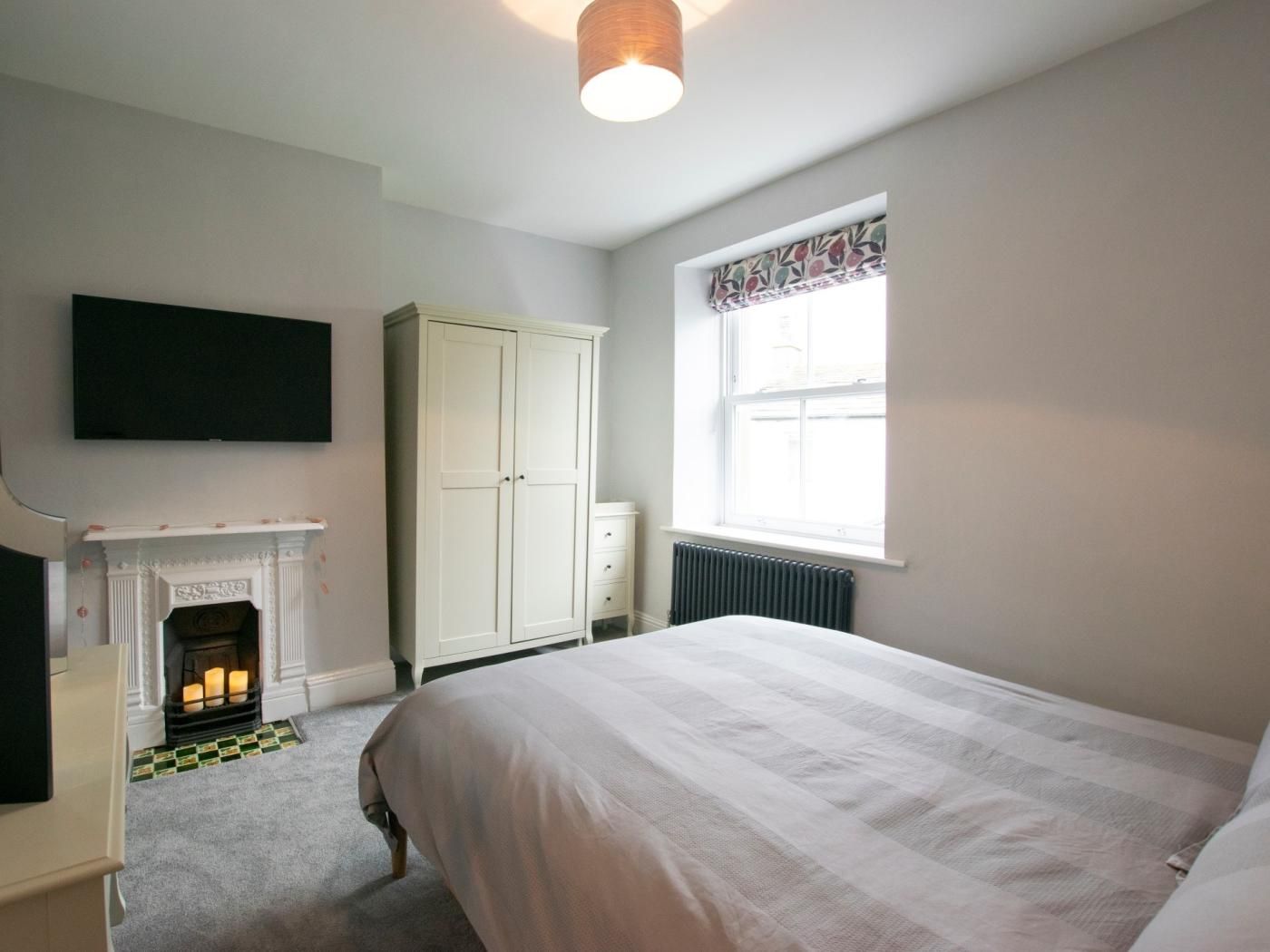 A bedroom with a bed, a wardrobe, a fireplace, a radiator, and a window with curtains.