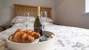 En seng med blomstret sengetæppe, et bakke med croissanter og en flaske vin, samt to tomme vinglas.