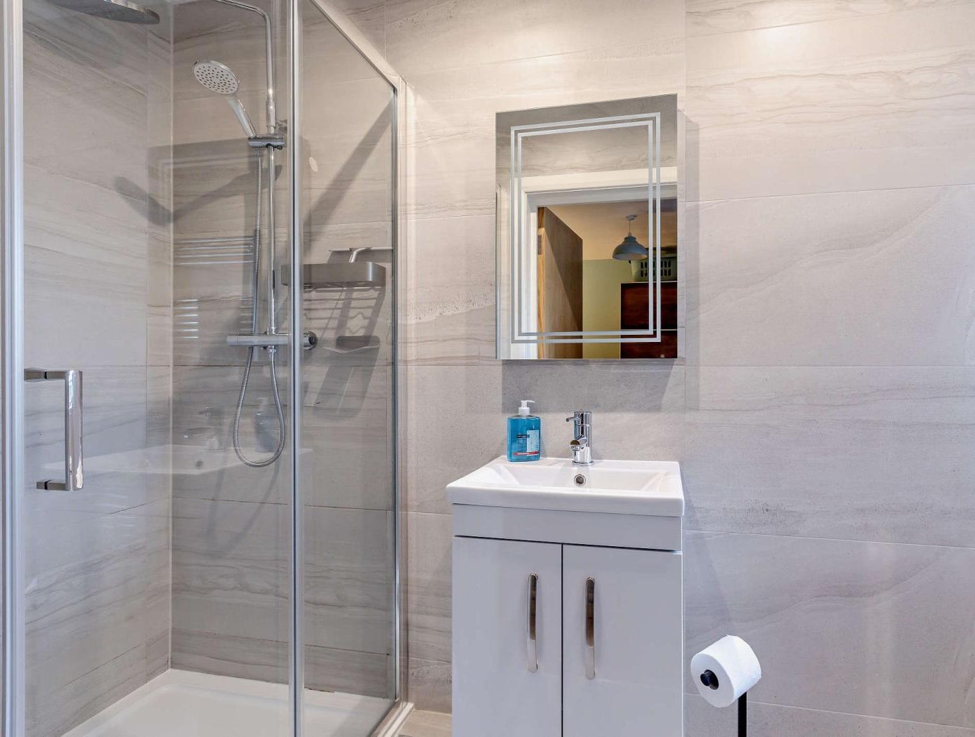 A modern bathroom with a glass-enclosed shower, a white sink with a mirror above it, and a toilet paper holder.