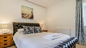 A bedroom with a large bed, two bedside tables, a radiator, and a window with curtains. - 3 Bed in Hayle (oc-fodry) (Saint Erth)