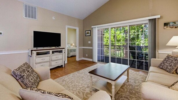 A living room with a flat-screen TV, a white dresser, a sofa, a coffee table, and a sliding glass door leading to an outdoor area. - Unwind At The Riverwalk, Spacious 2BR Retreat (Myrtle Beach)