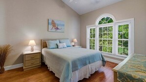 A bedroom with a bed, bedside tables, a window with blinds, a ceiling fan, and a painting on the wall. - Unwind At The Riverwalk, Spacious 2BR Retreat (Myrtle Beach)