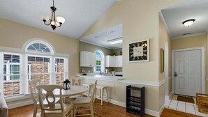 A spacious kitchen with a dining area, large windows, and a clock on the wall. - Unwind At The Riverwalk, Spacious 2BR Retreat (Myrtle Beach)
