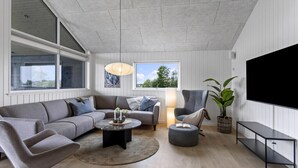 A modern living room with a grey sofa, a round coffee table, a side table, a floor lamp, a potted plant, and a large TV screen. - VillaVilla 955 - Skåstrup Strand, Fyn og øer (Bogense)