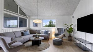 A modern living room with a grey sofa, a round coffee table, a side table, a floor lamp, a potted plant, and a large TV screen. - VillaVilla 955 - Skåstrup Strand, Fyn og øer (Bogense)