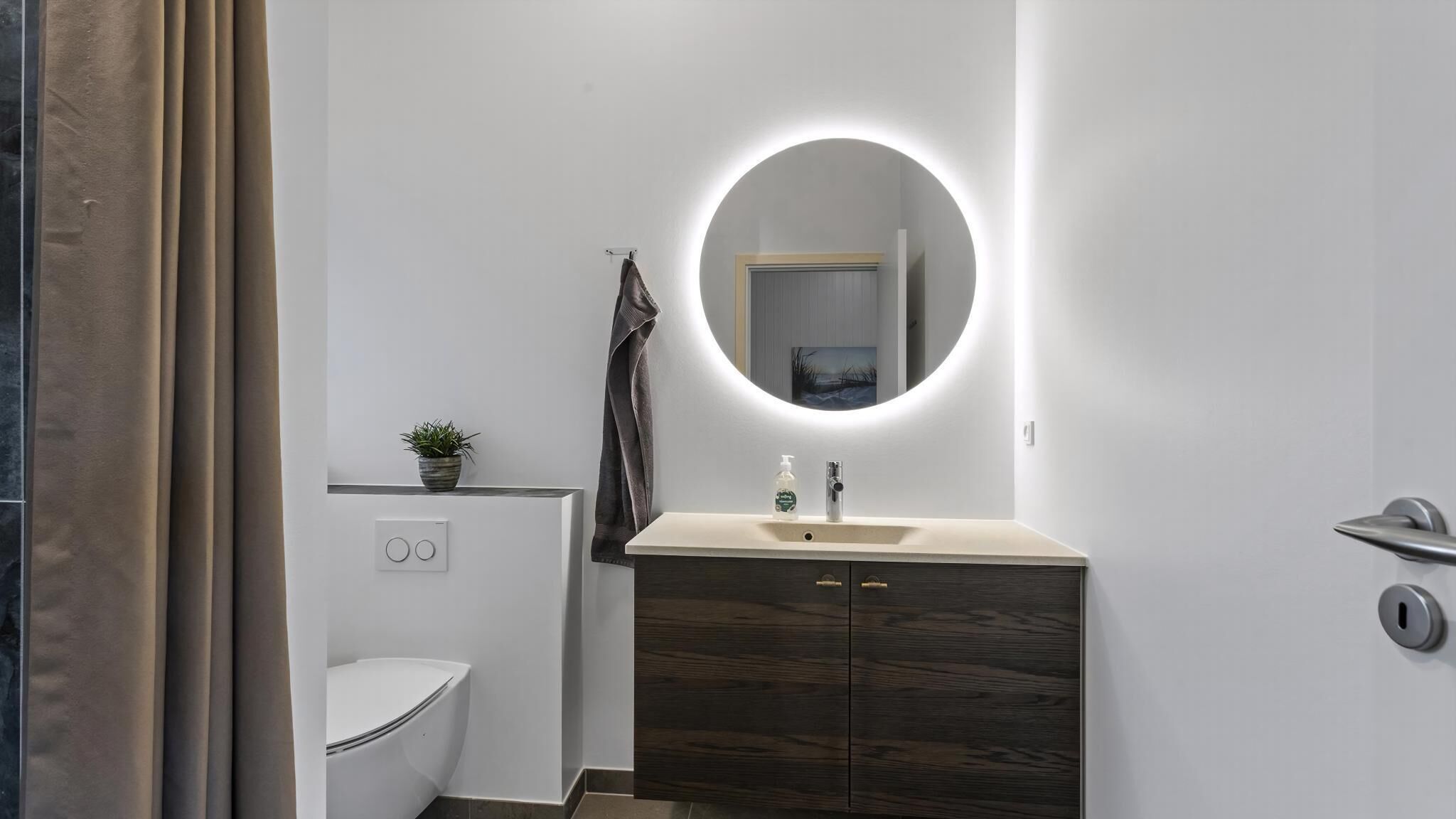 Een moderne badkamer met toilet, wastafel met spiegel en douche.