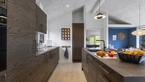 A modern kitchen with dark wood cabinets, a central island with bread and vegetables, and a view to the outdoors. - VillaVilla 955 - Skåstrup Strand, Fyn og øer (Bogense)