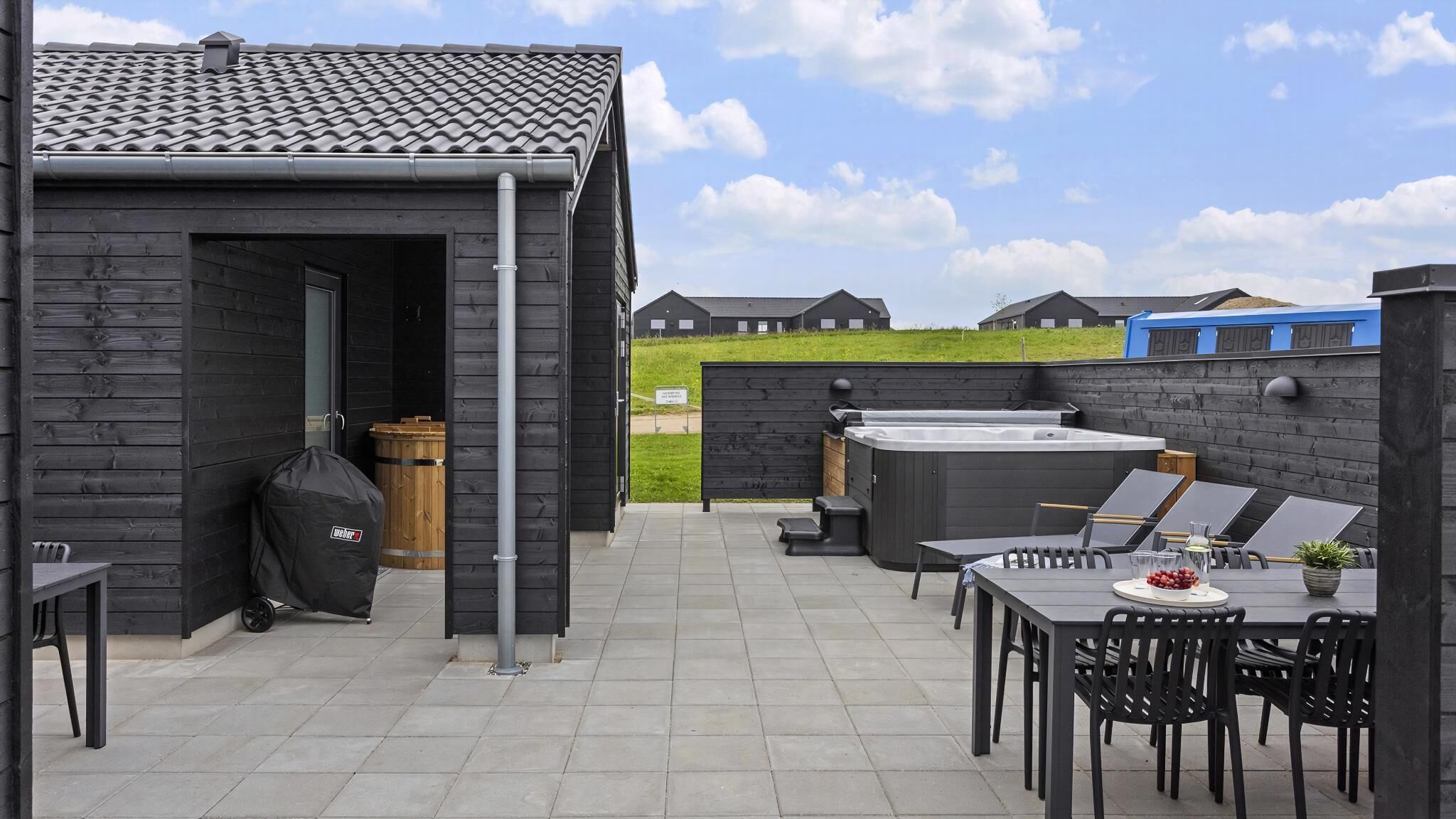 An outdoor patio with a hot tub, seating area, and a wooden structure.