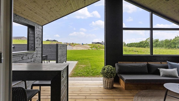 A modern outdoor seating area with a wooden deck, a black table, and a grey sofa with cushions. - VillaVilla 955 - Skåstrup Strand, Fyn og øer (Bogense)