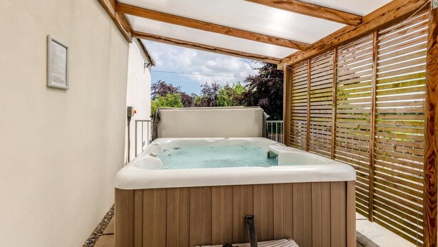 Un bain à remous situé dans un espace extérieur abrité, doté de poutres en bois et offrant une vue sur la verdure.