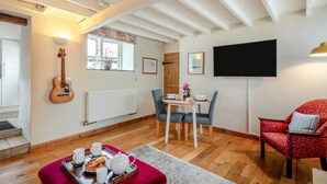Een gezellige woonkamer met een eethoek, een gitaar, een televisie en een rode fauteuil.
