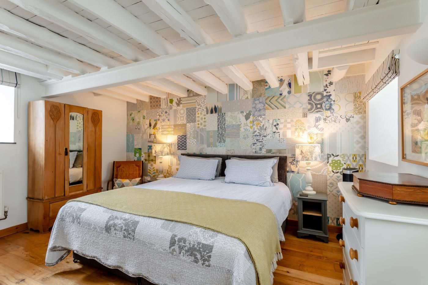 A bedroom with a large bed, wooden wardrobe, and a patterned wall.