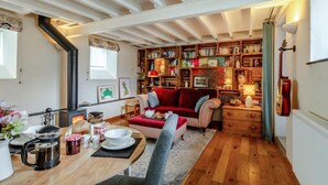 Een gezellige woonkamer met een open haard, een boekenkast, een eethoek met een tafel gedekt voor twee personen en een rode bank.