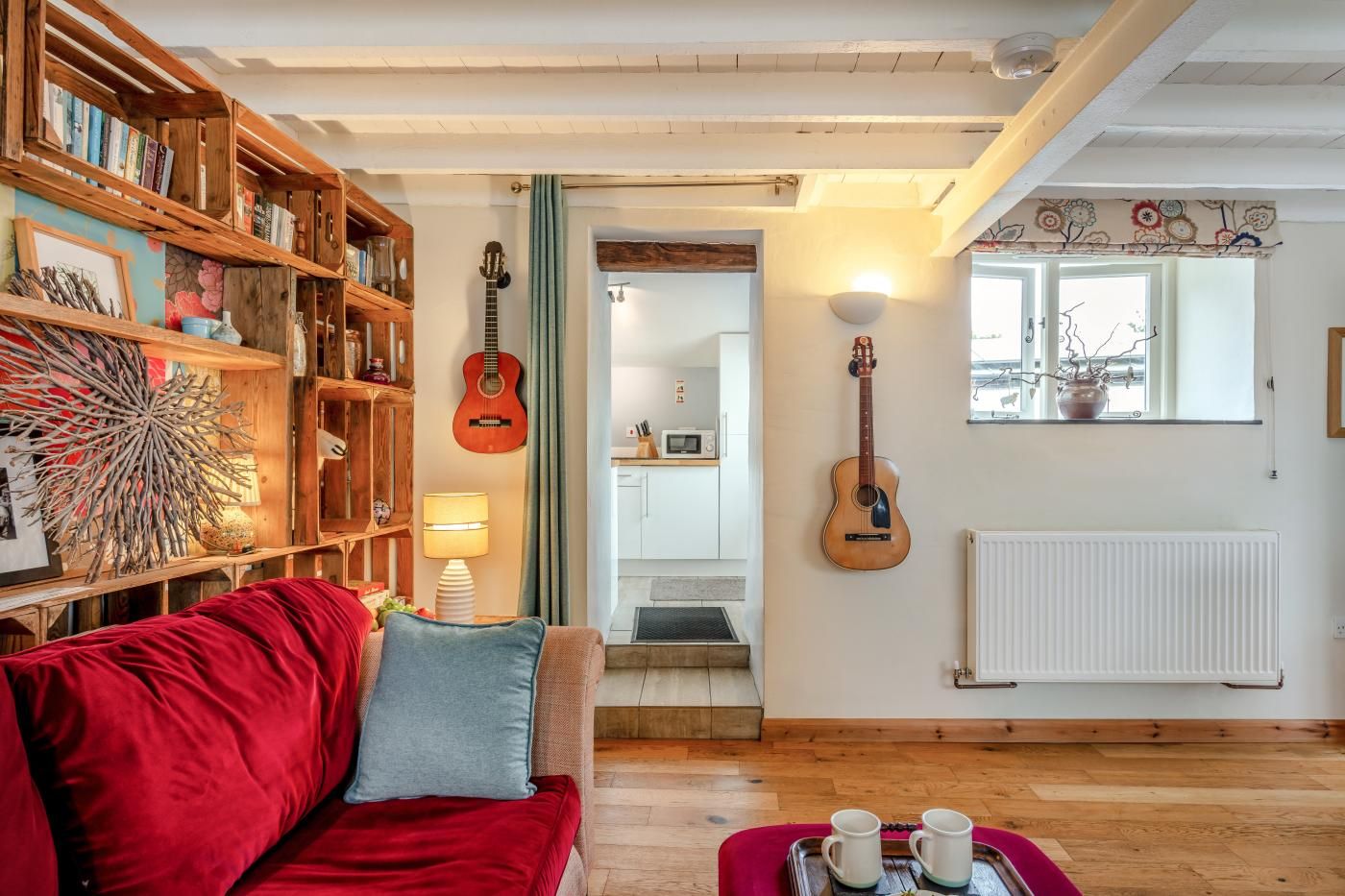 A cozy living room with a red sofa, a wooden bookshelf, and a guitar wall-mounted.