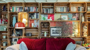 Een knus woongedeelte met een rode fluwelen bank, houten boekenkasten vol boeken en decoratieve objecten, en een vintage radio.