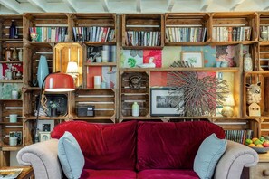 A cozy living room with a red velvet sofa, wooden bookshelves filled with books and decorative items, and a vintage radio. - 1 Bed in Umberleigh (oc-55321) (High Bickington)
