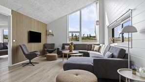 Een moderne woonkamer met een hoekbank, een flatscreen televisie en een groot raam met uitzicht op het landschap.