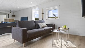 Ein modernes Wohnzimmer mit einem grauen Sofa, einem kleinen runden Tisch und Blick ins Freie durch ein Fenster.
