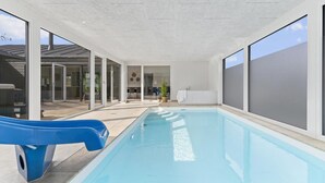 Ein Hallenbad mit einer blauen Rutsche, großen Fenstern und Blick ins Freie.