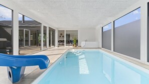 An indoor swimming pool with a blue slide, large windows, and a view of the outside. - VillaVilla 967 - Bønnerup Strand, Østjylland (Glesborg)
