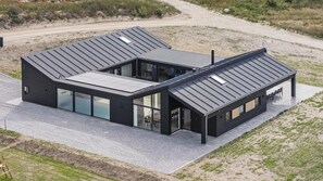 Een modern huis met twee verdiepingen, een plat dak, grote ramen en een verharde oprit.