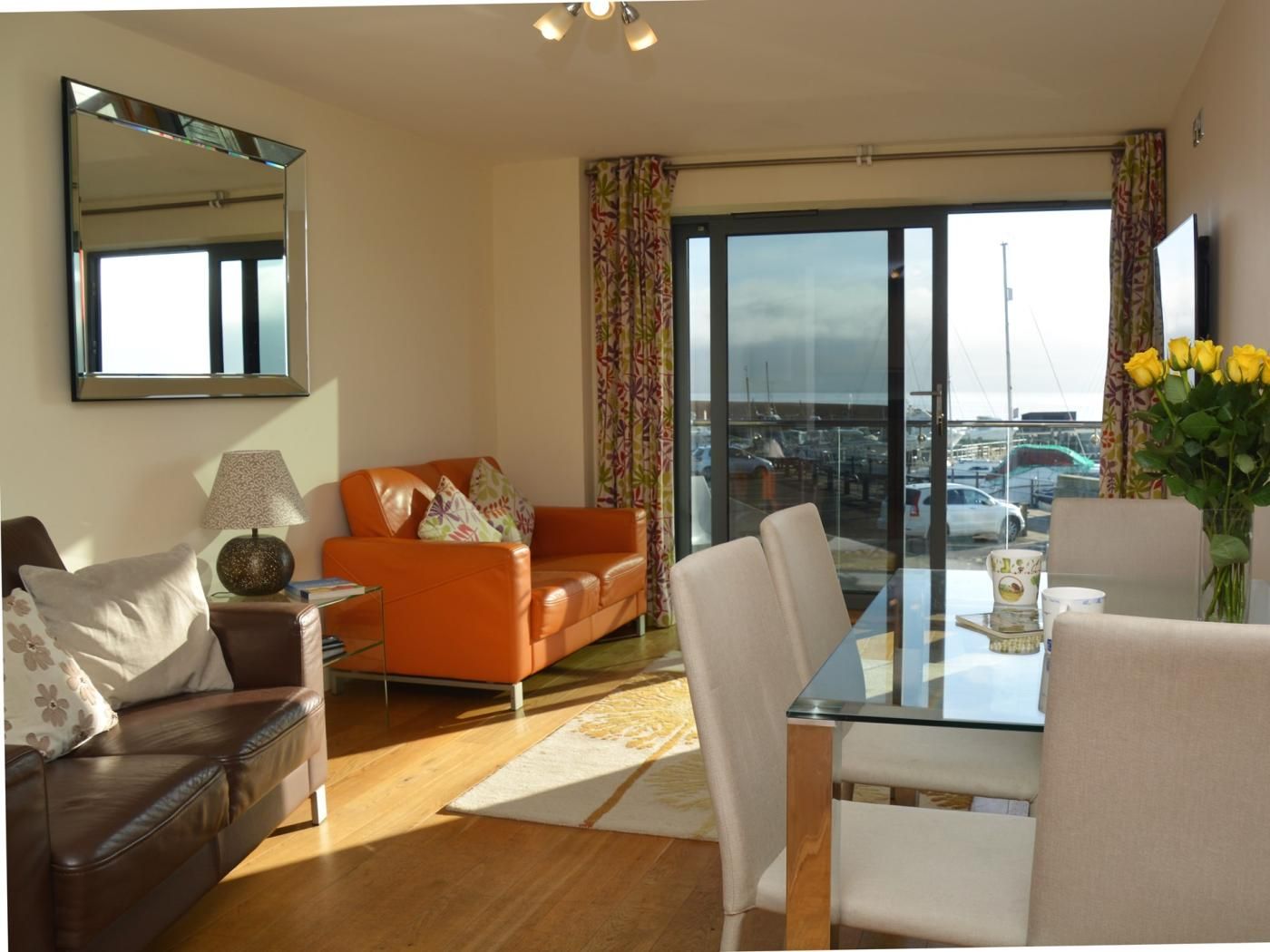 A modern living room with a glass table, leather sofas, and a large window with curtains.