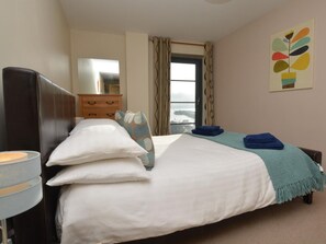 Ein Schlafzimmer mit Bett, Kommode, einem Fenster mit Vorhängen und einem Bild an der Wand.