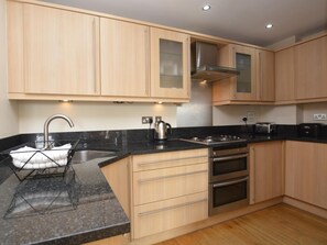 A modern kitchen with wooden cabinets, a stainless steel sink, a gas stove, and a built-in oven. - 2 Bed in Bridport (oc-pebba) (West Bay)