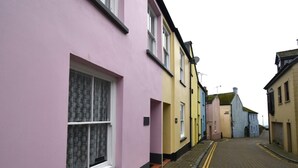 A narrow street with colorful buildings, a paved road, and a yellow double yellow line marking. - 3 Bed in Tenby (oc-fb141) (Tenby)