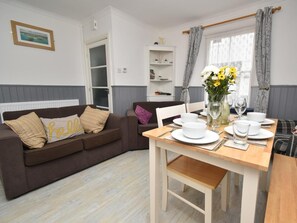 A dining area with a wooden table set for two, white plates, and a vase with flowers. - 3 Bed in Tenby (oc-fb141) (Tenby)