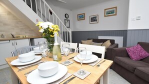 A dining area with a wooden table set for four, a vase of flowers, and a bottle of champagne. - 3 Bed in Tenby (oc-fb141) (Tenby)