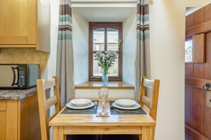 A dining area with a wooden table, chairs, a vase with flowers, and a window with curtains. - 1 Bed in Weston-super-mare (oc-45568) (Bleadon)