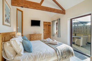 A bedroom with a bed, a dresser, a television, and a sliding glass door leading to an outdoor patio. - 1 Bed in Weston-super-mare (oc-45568) (Bleadon)