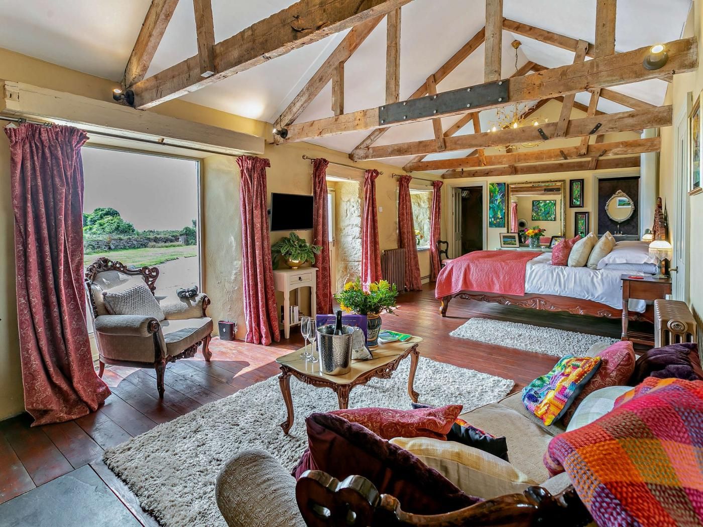 A spacious room with a large bed, a sitting area with a sofa and armchairs, and a view of the outdoors.