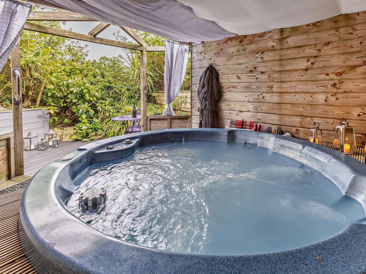 Ein Whirlpool vor einer Holzwand, umgeben von viel Grün.