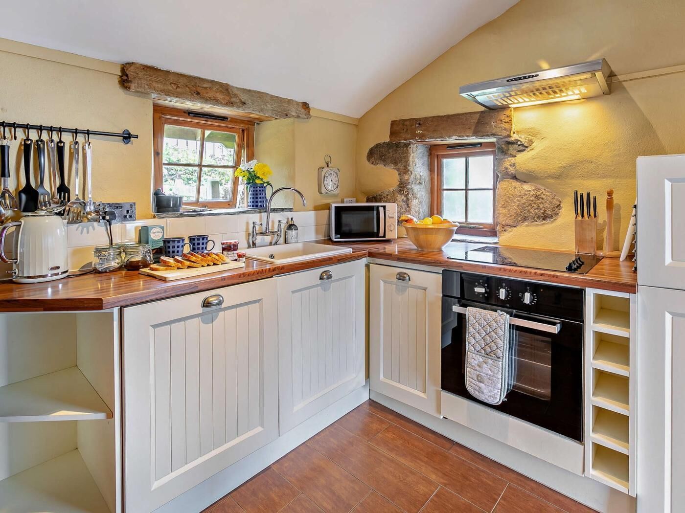 A kitchen with white cabinets, a wooden countertop, a stove, a microwave, and a sink.