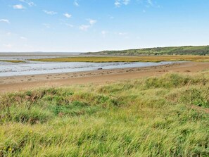 A coastal landscape with a sandy beach, grassy dunes, and a distant hill. - 1 Bed in Weston-super-mare (oc-93383) (Kewstoke)