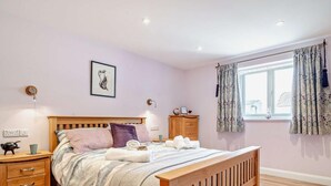 Une chambre à coucher avec un lit en bois, des tables de chevet, une commode, une fenêtre avec des rideaux et un tableau accroché au mur.