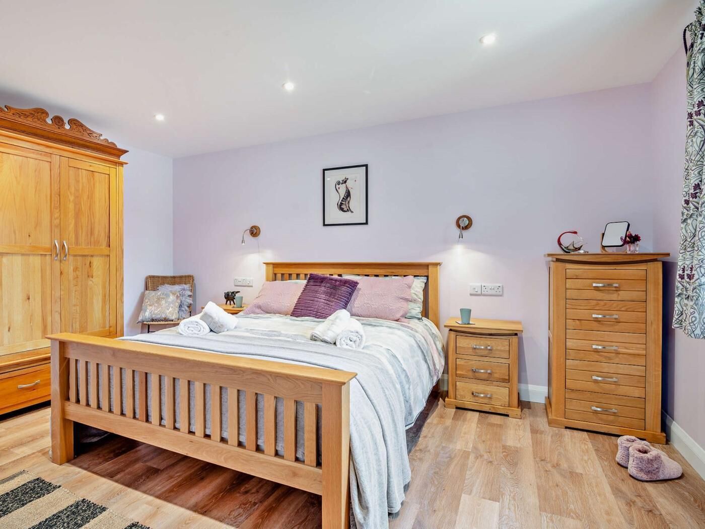 A bedroom with a wooden bed, bedside tables, a wardrobe, and a wall-mounted picture.