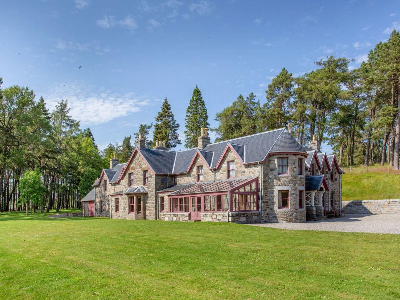 A stone building with multiple gabled roofs, surrounded by a grassy area and tall trees.