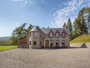 Ein Gebäude aus Stein mit einem zentralen Eingang, zahlreichen Fenstern und einer Schotterauffahrt.