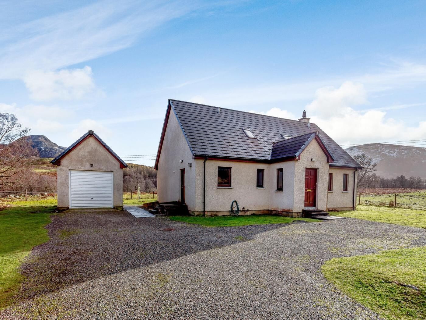 Une maison à deux étages avec une allée en gravier et un petit garage.