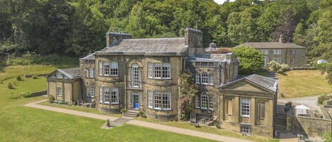 A large, historic stone building with multiple wings and a well-maintained lawn.