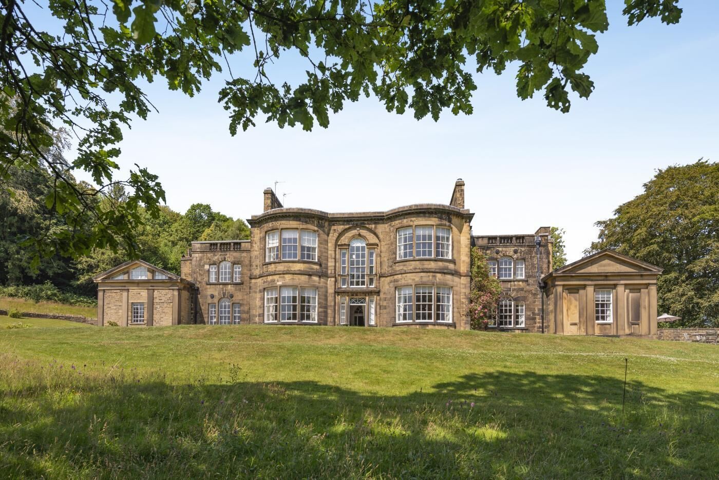 A large, historic stone building with multiple windows and a symmetrical facade, surrounded by a well-maintained lawn.