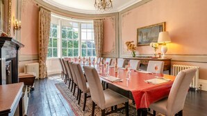 Un comedor formal con una larga mesa dispuesta para una comida, rodeada de sillas, un candelabro y una chimenea.